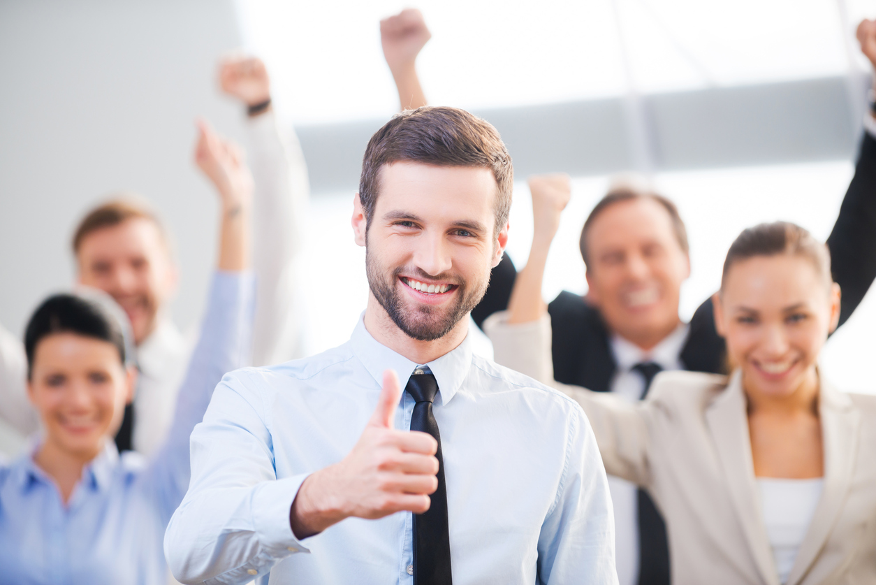 Happy businessman showing his thumb up and smiling while his colleagues standing in the background